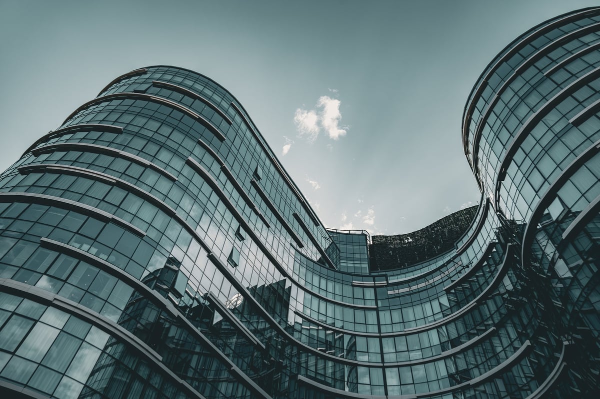 Low angle view of a contemporary glass office complex with sweeping curved facades and reflective windows. Modern corporate architecture symbolizing innovation, urban development, engineering excellence and business growth.